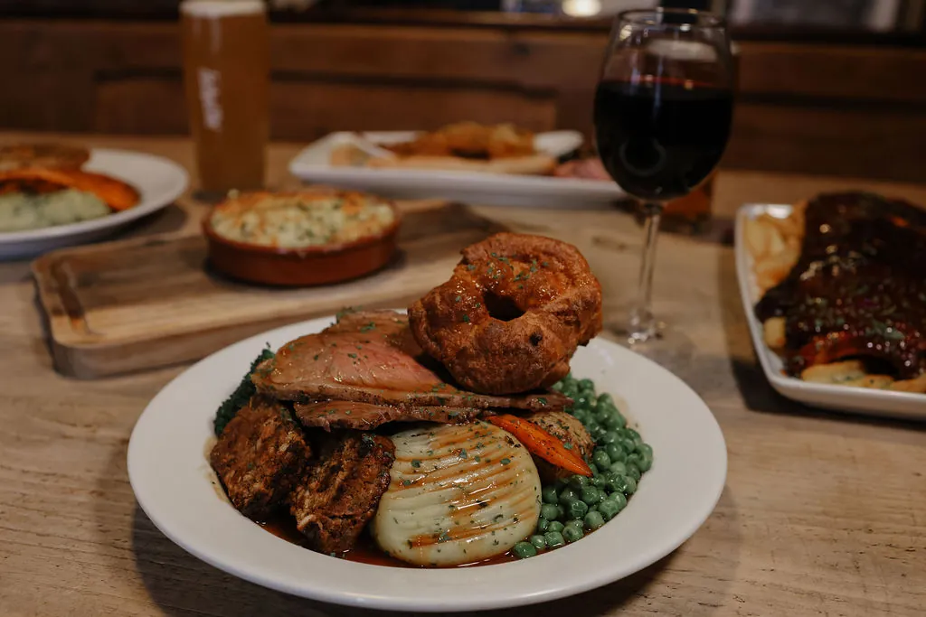 A Sunday roast with a Yorkshire pudding, sliced beef, mash, peas and carrots