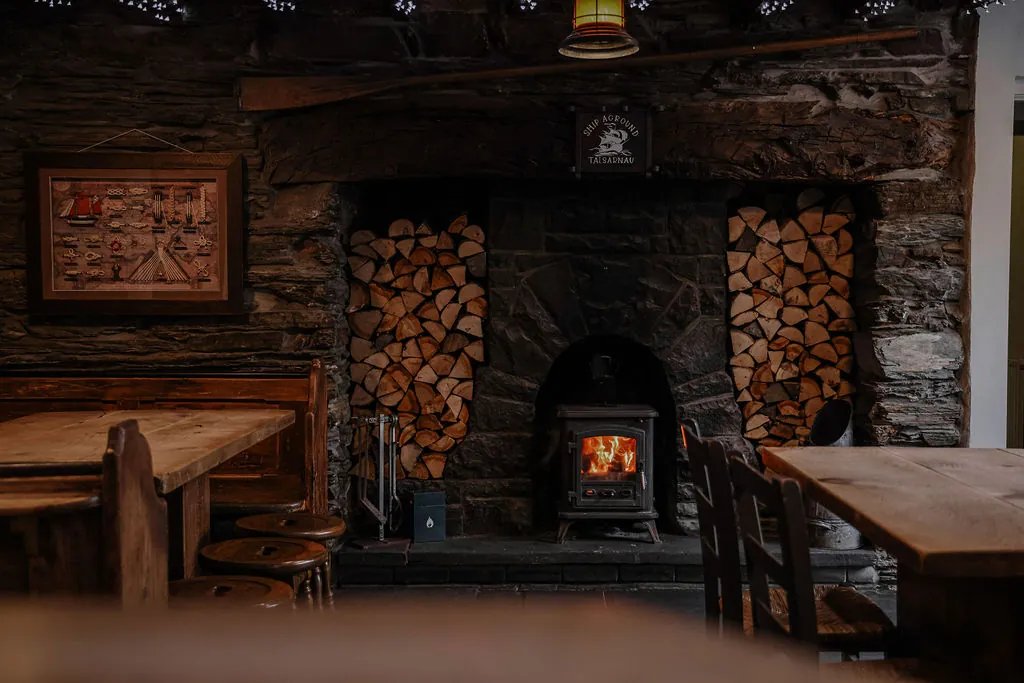 The cosy interior of The Ship Aground, warm lamplight over slate walls and a wood-burning stove
